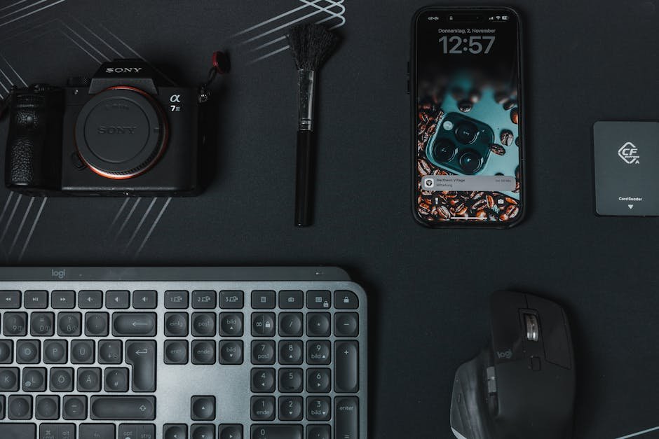 Flat lay of modern electronics including a camera, smartphone, and keyboard on a stylish black surface.