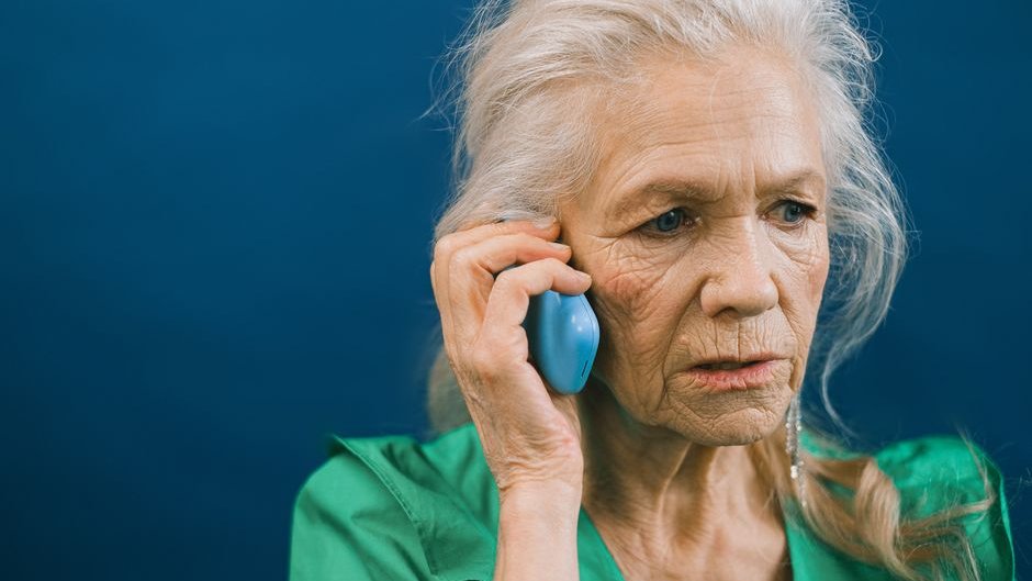 A grandmother listens to a phone call as an AI-generated voice convincingly tricks her into transferring money in under three seconds