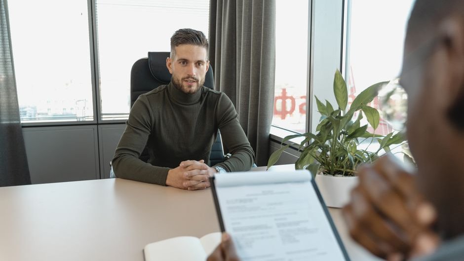 A graduate reviews a job listing on a laptop as AI-generated text fills the screen showing limited opportunities in a competitive market
